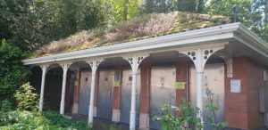 A block of toilets with metal doors. Moss and vegetation grows from the roof.