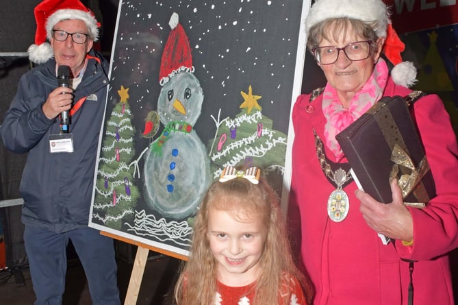 Clinton Rogers and Mayor Janet Lloyd pose with Luna-Alora and her winning Christmas Card Design, a snowman and Christmas Trees on a black background.